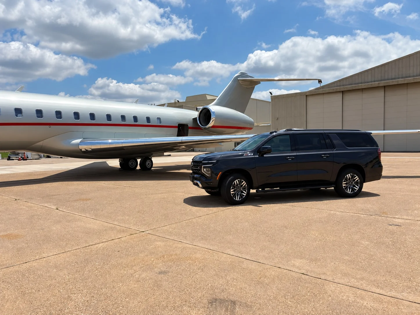 A black Chevrolet SUV parked alongside a private aircraft outside an airport hangar.