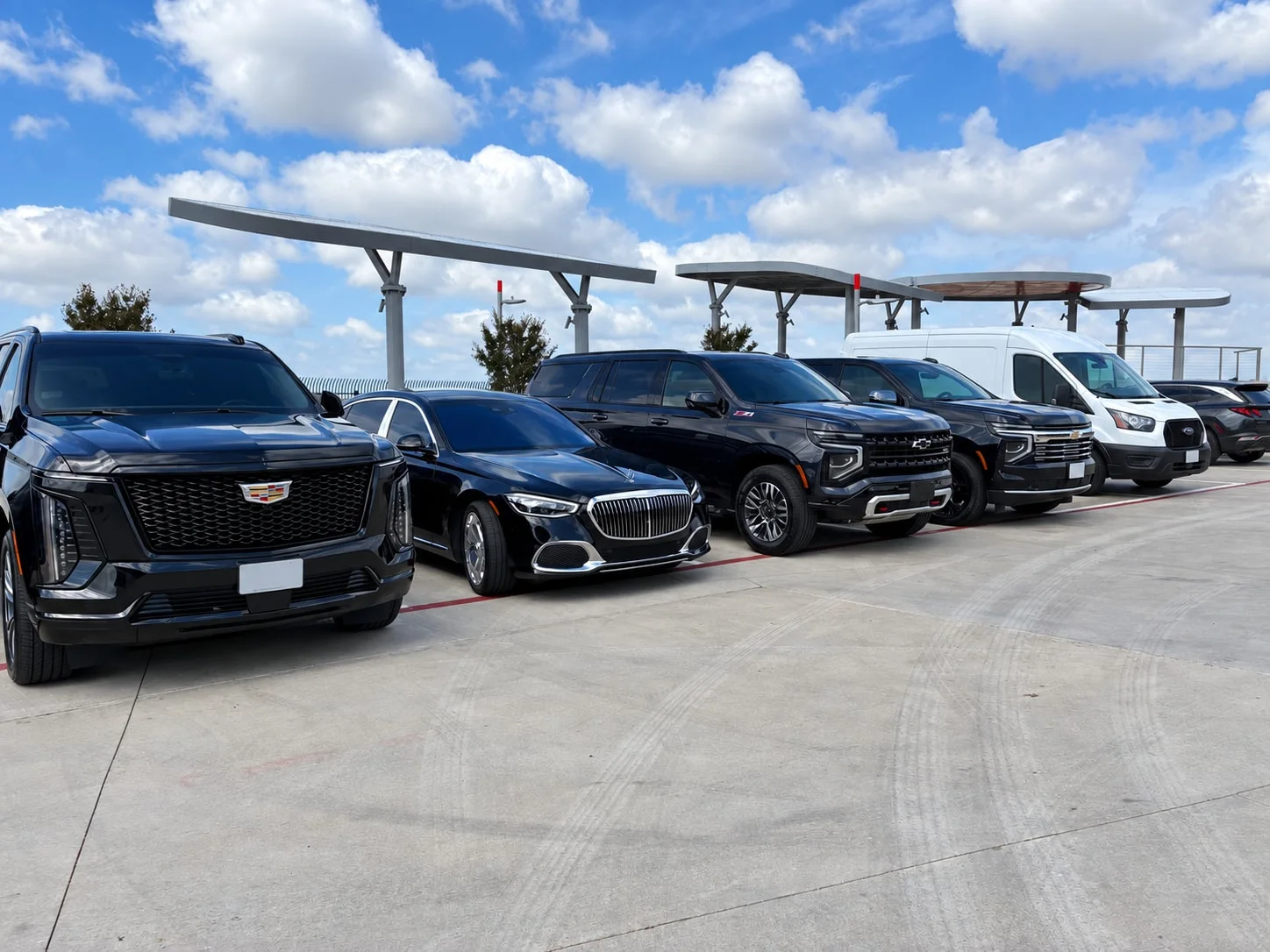 Black sedans and SUVs with a white passenger van lined up at a transportation staging area.
