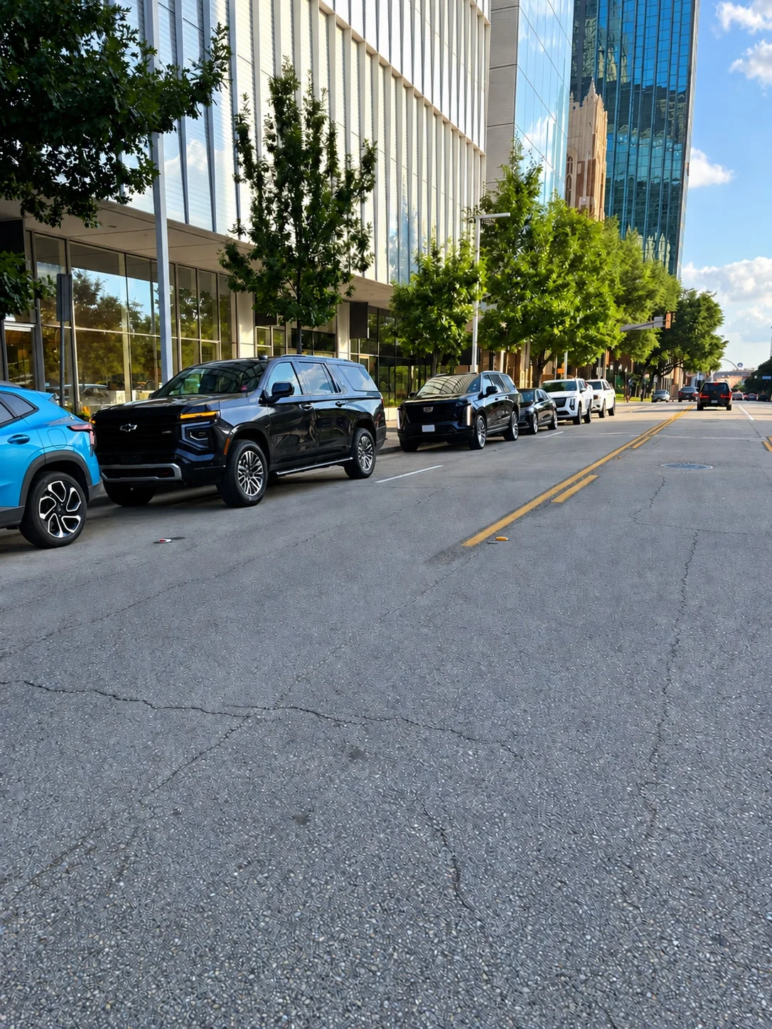 Black SUVs and a sedan parked along a downtown Dallas street.