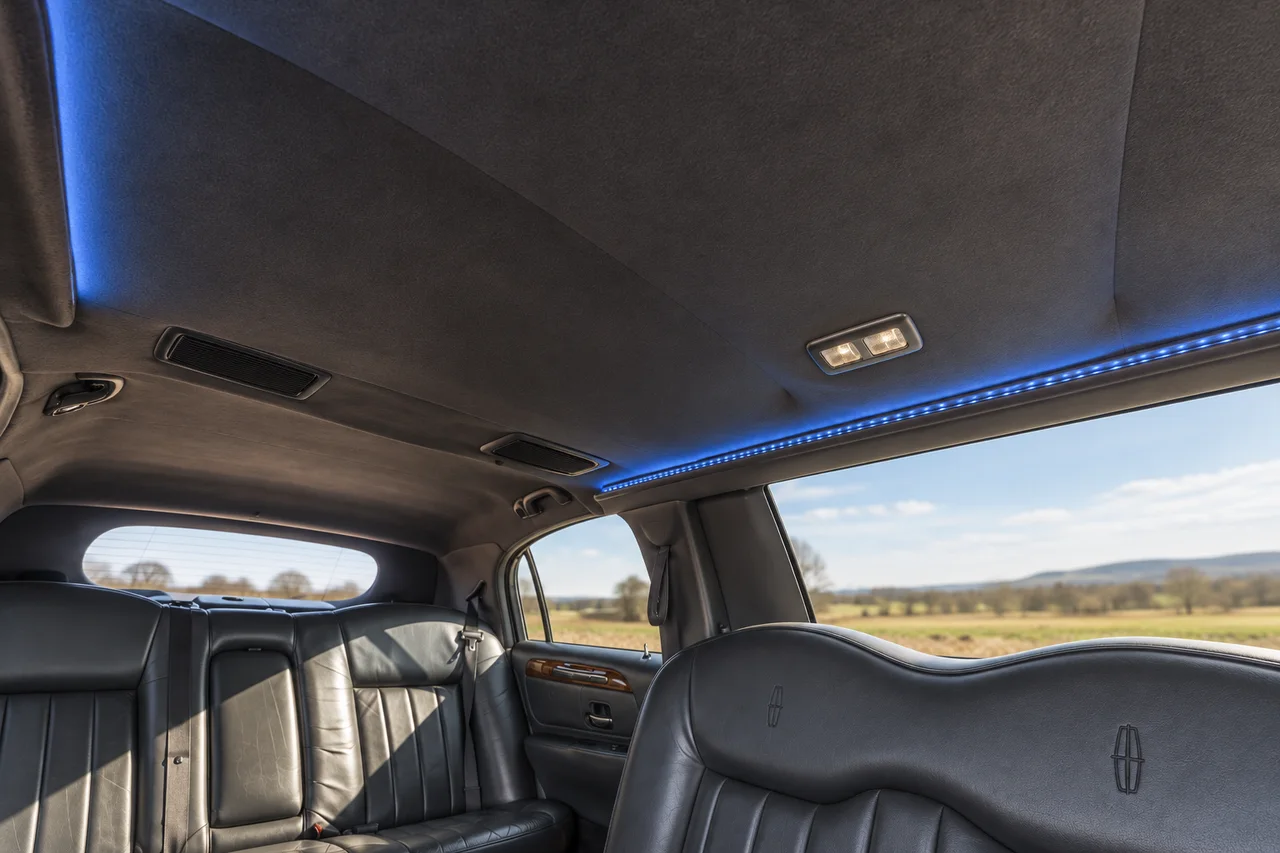 AI-recreated Lincoln limousine headliner detail with charcoal upholstery, dome lighting, ventilation grilles and thin blue lighting along the window edge.